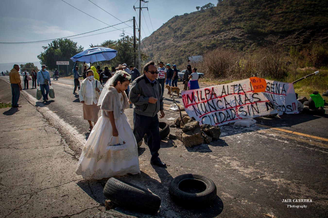 Una niña camina con su padre después de salir de una iglesia en San Pedro Atocpan, mientras que habitantes mantenían bloqueada la carretera en protesta por la privatización del agua.Diciembre 2022