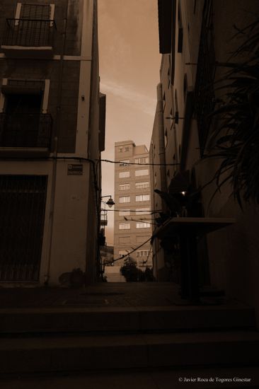Calle angosta con un edificio al fondo y sombras.