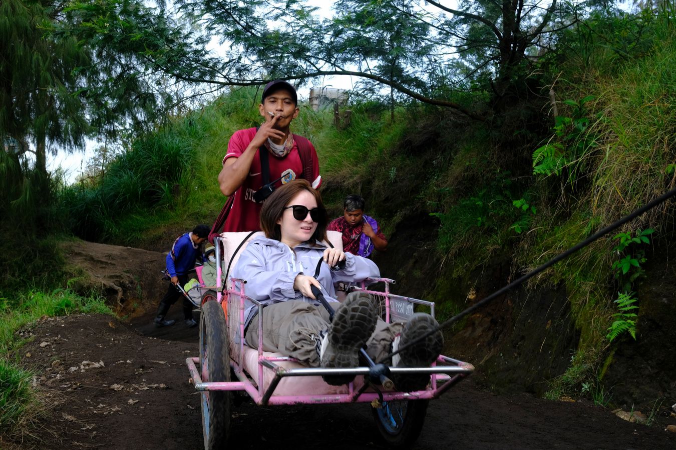 A porter smokes while pushing a wheelbarrow with a tourist on their way to the top of Ijen volcano