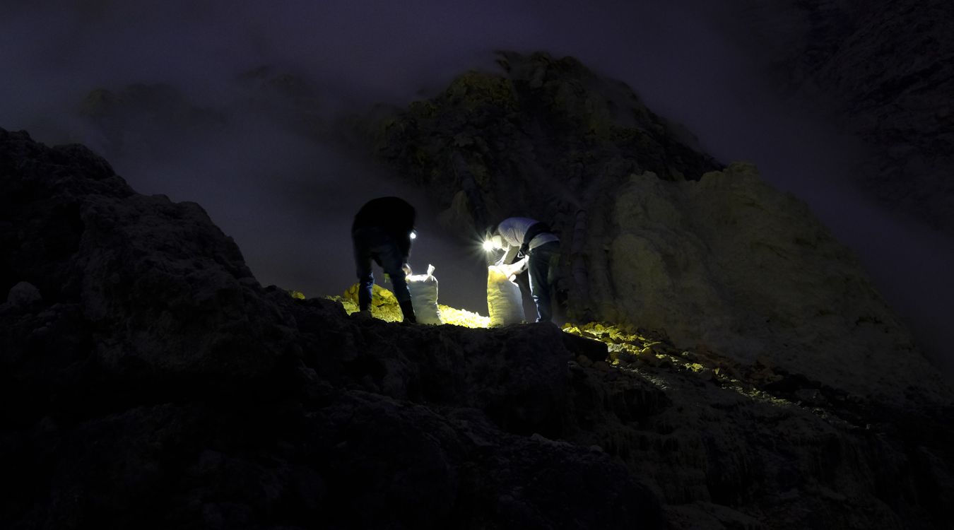 At night, two miners fill sacks with sulfur in the crater of the Ijen volcano