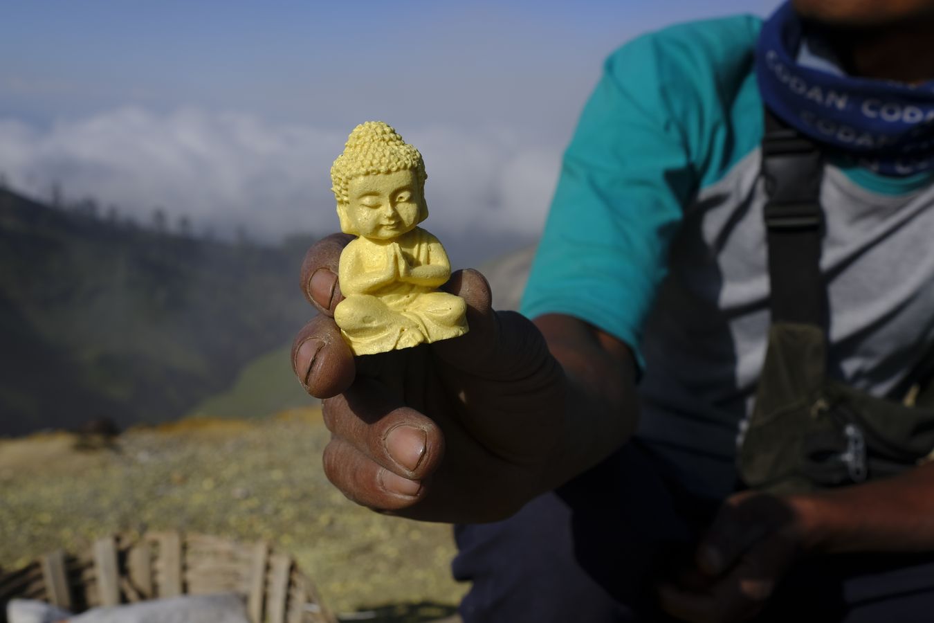 Miner shows a small Buddha carving made of sulfur, create as a souvenir to sell to tourists