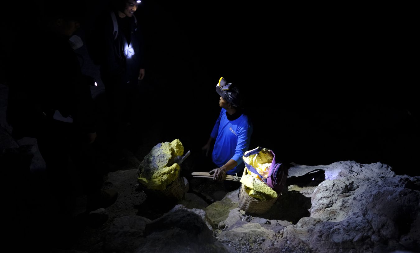 Miner talks to tourists during a short break on the way up to the crater of the Ijen volcano, carrying baskets full of sulfur