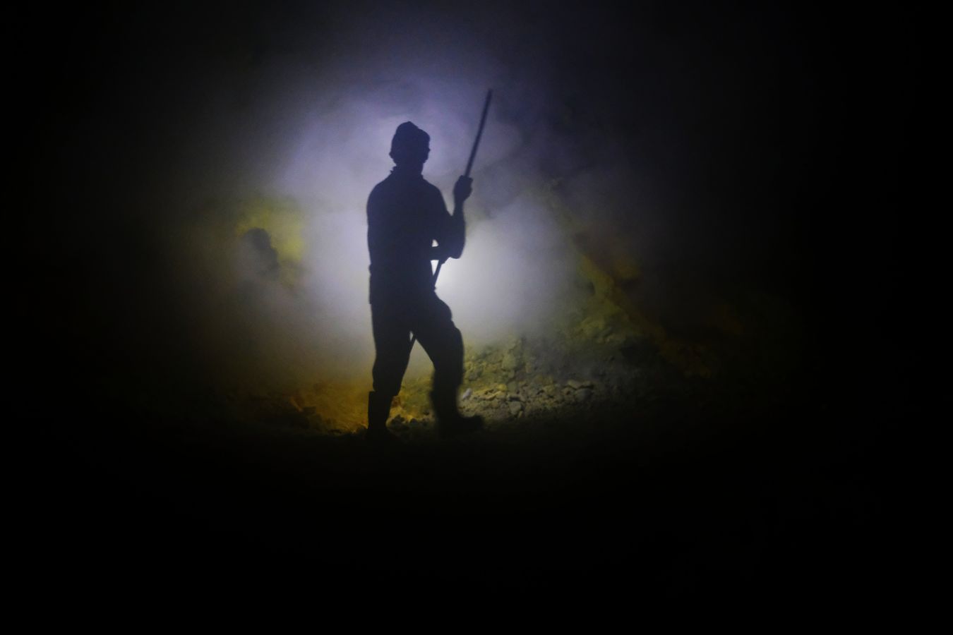 Miner extracts large stones of sulfur using a metal bar, in the crater of the Ijen volcano