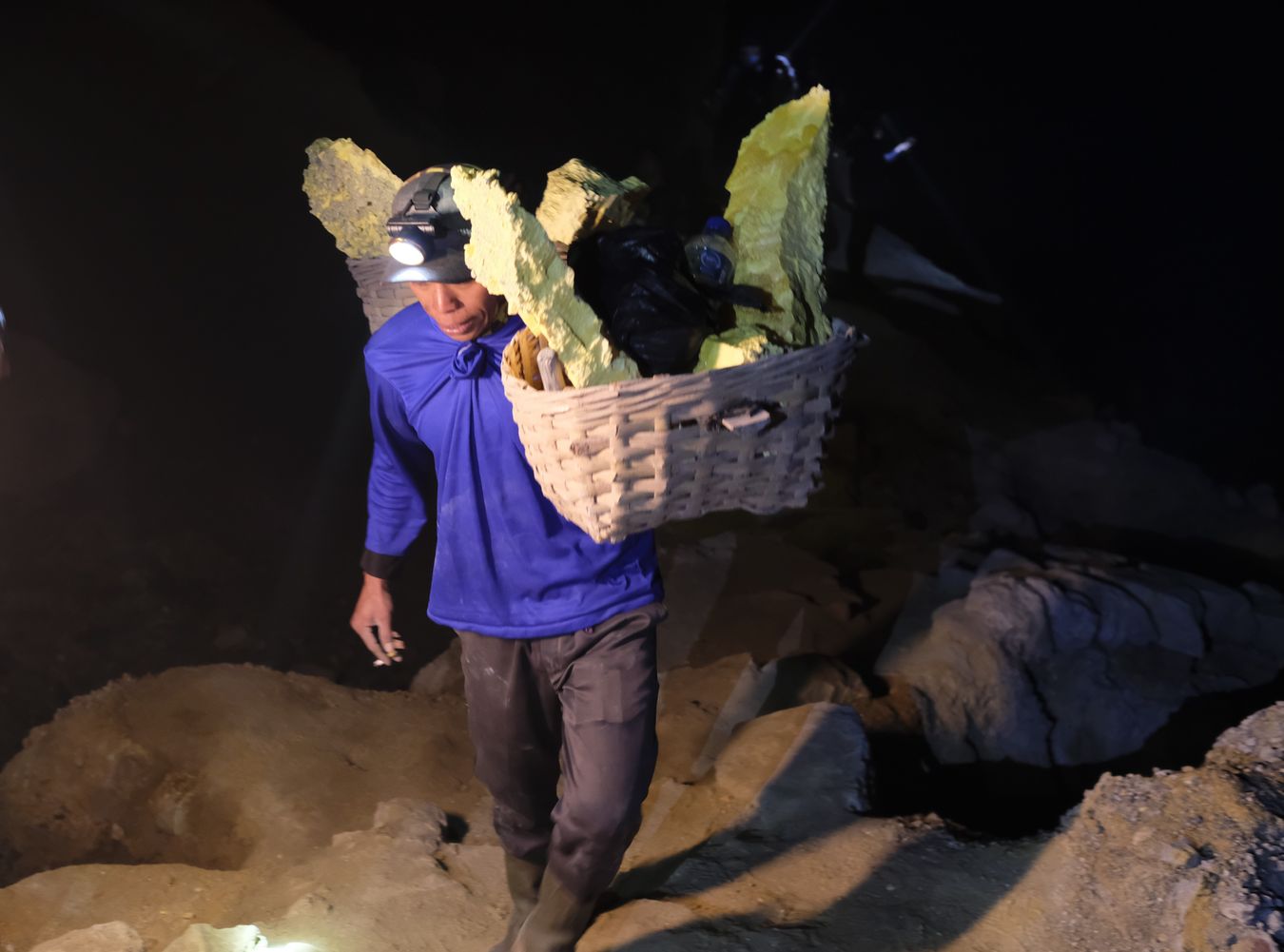 Miner ascending from the crater of the Ijen volcano with traditional baskets loaded with sulfur