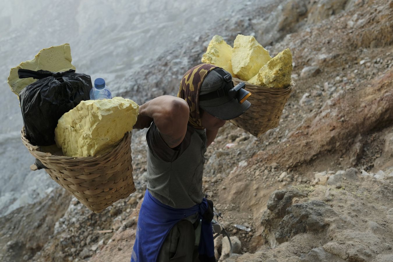 Miner ascending from the crater of the Ijen volcano with traditional baskets loaded with sulfur