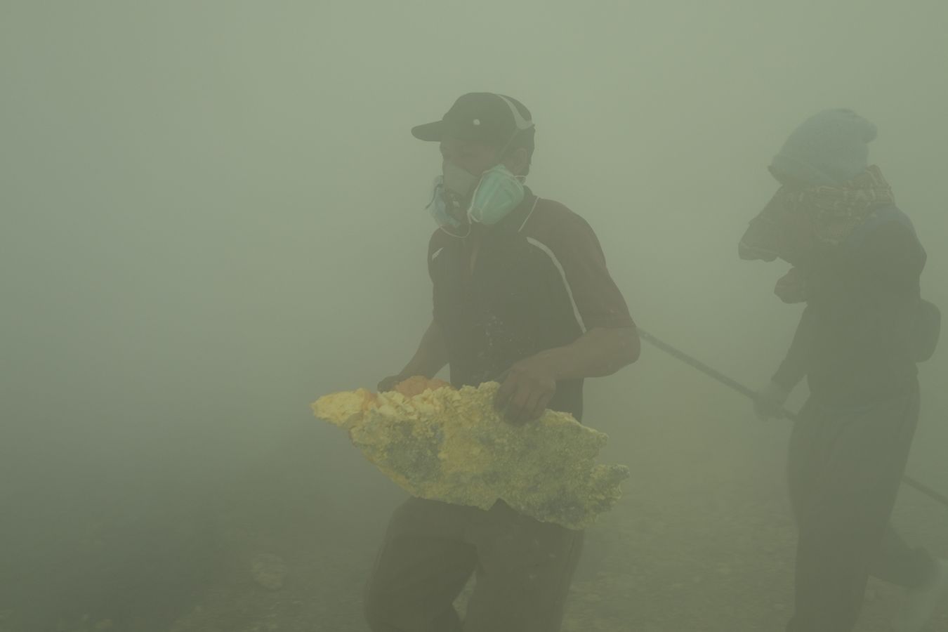 Smoke-shrouded miners carry a large boulder of sulfur recently extracted from the crater of the Ijen volcano