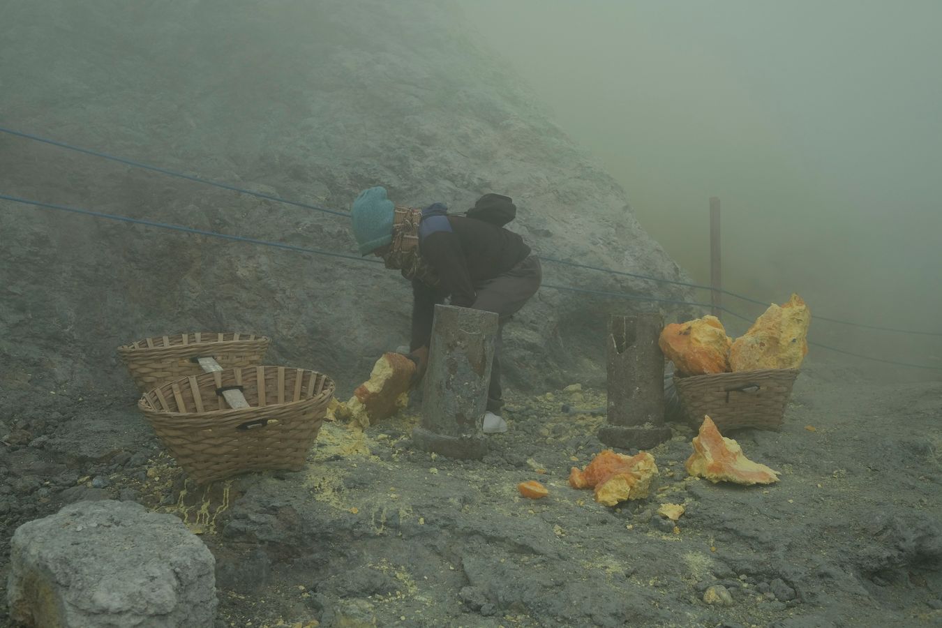 A smoke-shrouded miner in the crater of the Ijen volcano, fills traditional baskets with previously mined sulfur stones