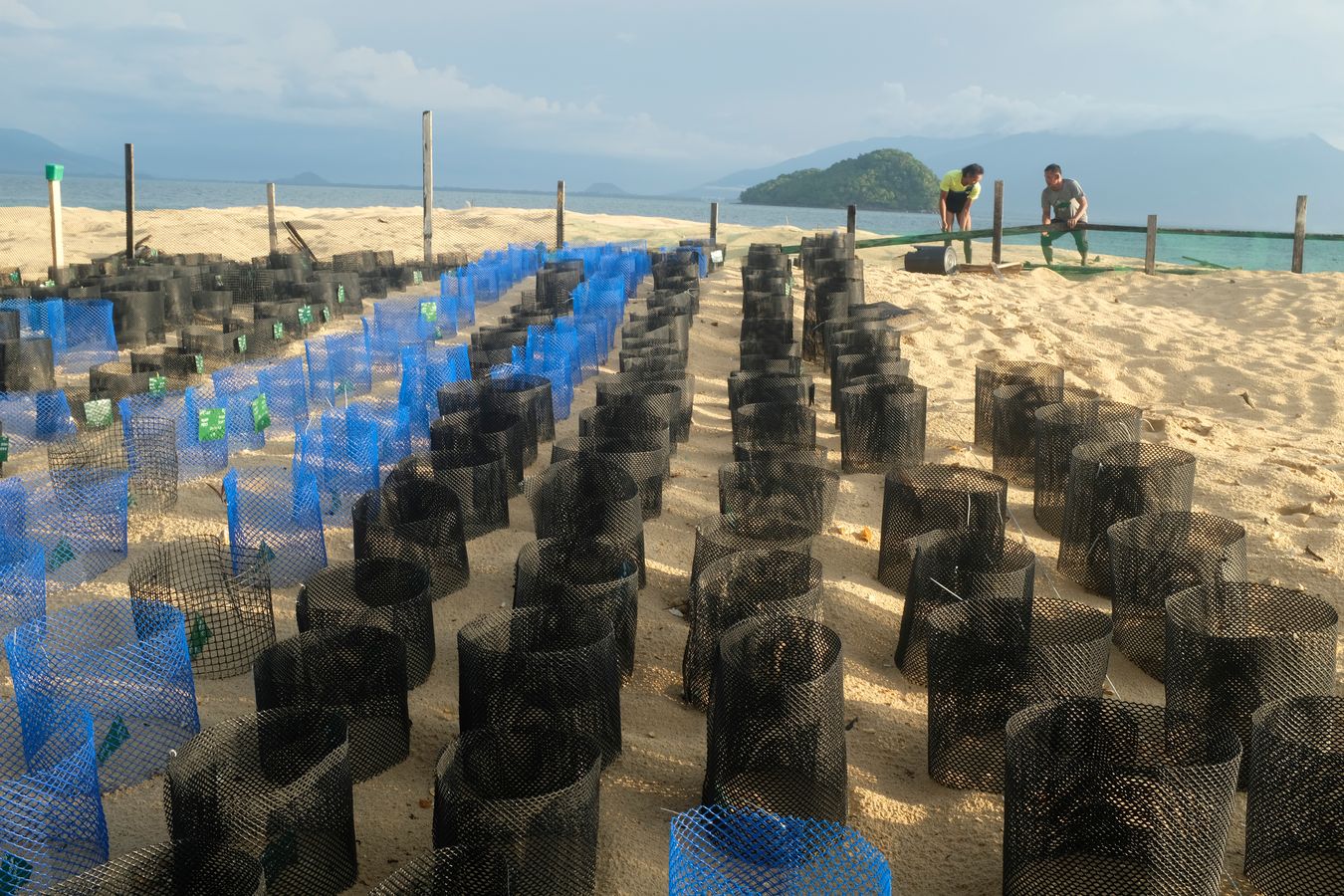 View of the sea turtle hatchery and two rangers carrying out maintenance and repair work, with the small island of Talang Kecil in the background.