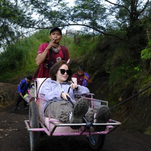 A porter smokes while pushing a wheelbarrow with a tourist on their way to the top of Ijen volcano