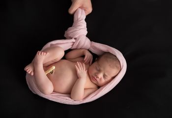 newborn sobre fondo negro y tela rosa anudada