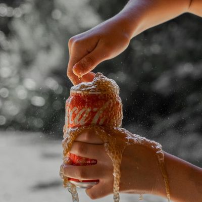 Manos de niña abriendo una coca-cola derramándose el líquido