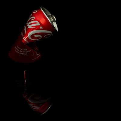 Lata de coca-cola aplastada sobre fondo negro con su reflejo proyectado