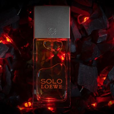 Frasco de perfume colonia Solo De Loewe sobre cama de brasa y fuego