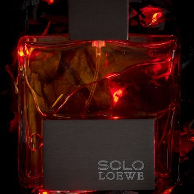 Frasco de perfume colonia Solo De Loewe sobre cama de brasa y fuego