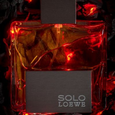 Frasco de perfume colonia Solo De Loewe sobre cama de brasa y fuego