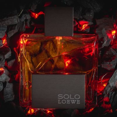 Frasco de perfume colonia Solo De Loewe sobre cama de brasa y fuego